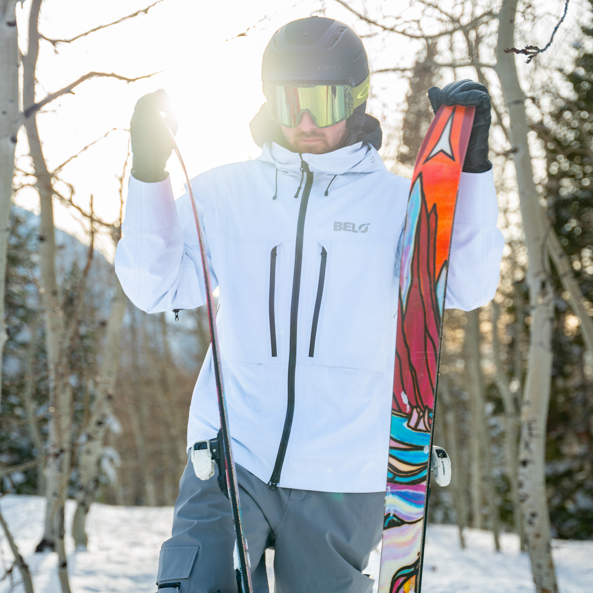 Person in ski gear holding a colorful ski in a snowy forest setting