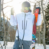 Person in ski gear holding a colorful ski in a snowy forest setting